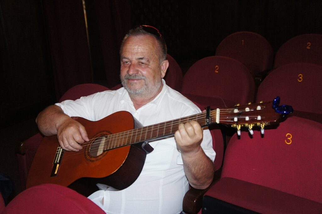 Zdjęcie wykonane podczas próby. W części dla widzów. Aktor z gitarą usiadł na jednym z miejsc dla widzów.