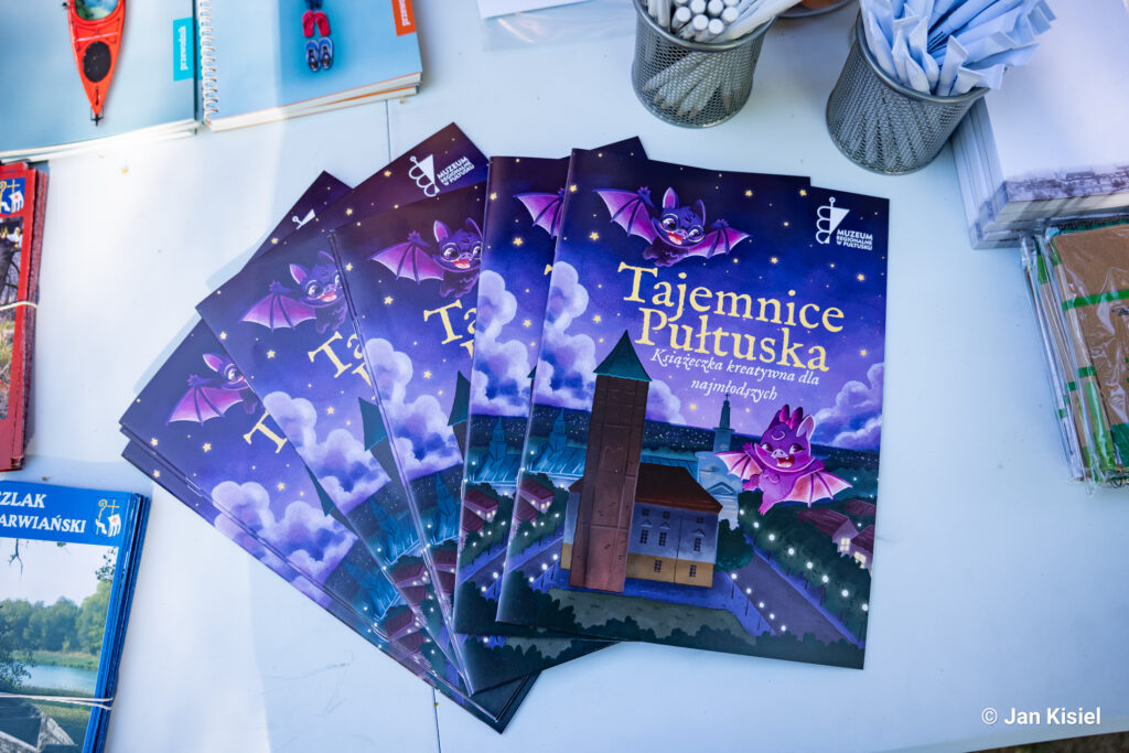 Kolorowe książeczki kreatywne „Tajemnice Pułtuska” z nietoperzami na okładce, przygotowane przez Muzeum Regionalne w Pułtusku, wyeksponowane na stoliku podczas wydarzenia edukacyjnego.