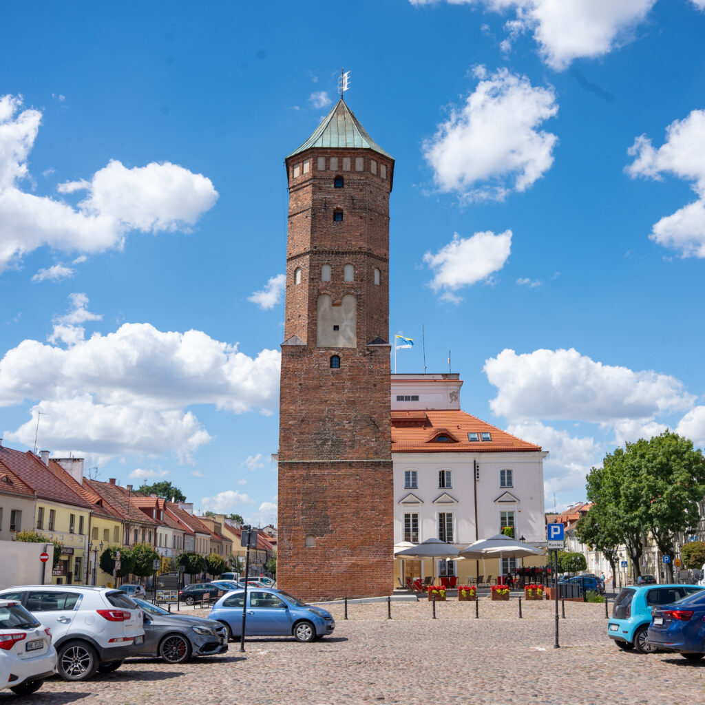 Zdjęcie kolorowe. Wieża ratuszowa w Pułtusku od strony zamku. W tle widoczny ratusz miejski.